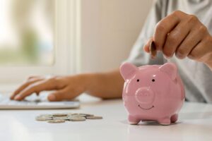 Persona che calcola dei rendimenti e mette una moneta in un salvadanaio