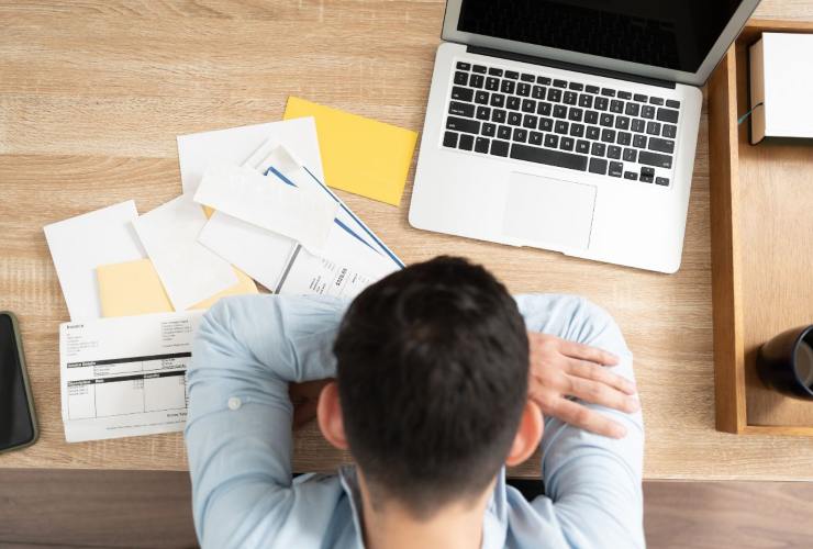 persona preoccupata per i debiti mentre consulta il pc e legge documenti