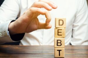 dadi con scritta DEBT (debiti) e mano che gioca con i dadi
